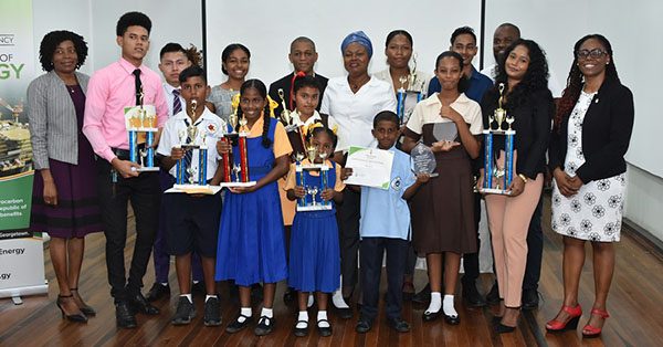 Winners in the Department of Energy’s Art and Logo Competition along with Director of the Department, Dr. Mark Bynoe (back row, centre), Chief Judge of the competition, Regina Torrington (second row, centre) along with the Officer Manager and Legal Adviser in the Department of Energy, extreme left and right respectively,  Sharon Patterson and Joanna Simmons at the National Gallery of Art, Castellani House. (Ministry of the Presidency photo)