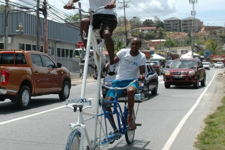 Leon Long peddles the high-rider bicycle from the top while Jahzeel Joseph steers the machine from the back, as the duo ride along the Western Main Road, Carenage.