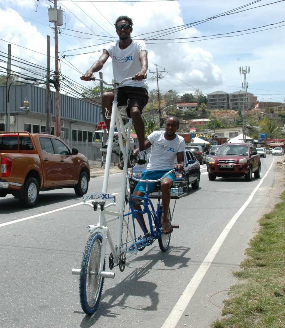 Leon Long peddles the high-rider bicycle from the top while Jahzeel Joseph steers the machine from the back, as the duo ride along the Western Main Road, Carenage.