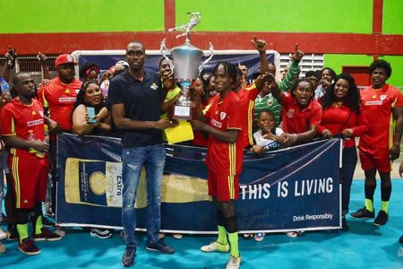 Champs at last- Tiger Bay captain and event’s MVP Deon Alfred receives the championship trophy from Corona Brand Manager Colin Stuart in the presence of team-mates and supporters after defeating Back Circle in the final at the National Gymnasium, Mandela Avenue