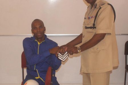From Corporal to Sergeant: Sergeant Clive Clarke (seated) being presented with his stripes by Commander of ‘A’ Division Marlon Chapman. (Guyana Police Force photo)