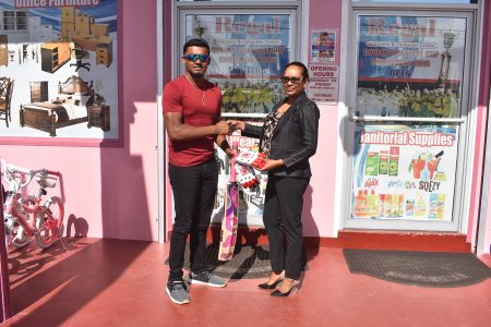 Alex Algoo (left) receives his gear from Regal Stationary Manager, Telesha Ousman.