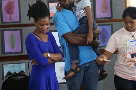 Proud artist: A child proudly showing her parents one of her pieces at a children’s art exhibition that was hosted on Friday at the Carifesta Sports Complex, following the conclusion of a two-week art workshop. (Terrence Thompson photo)