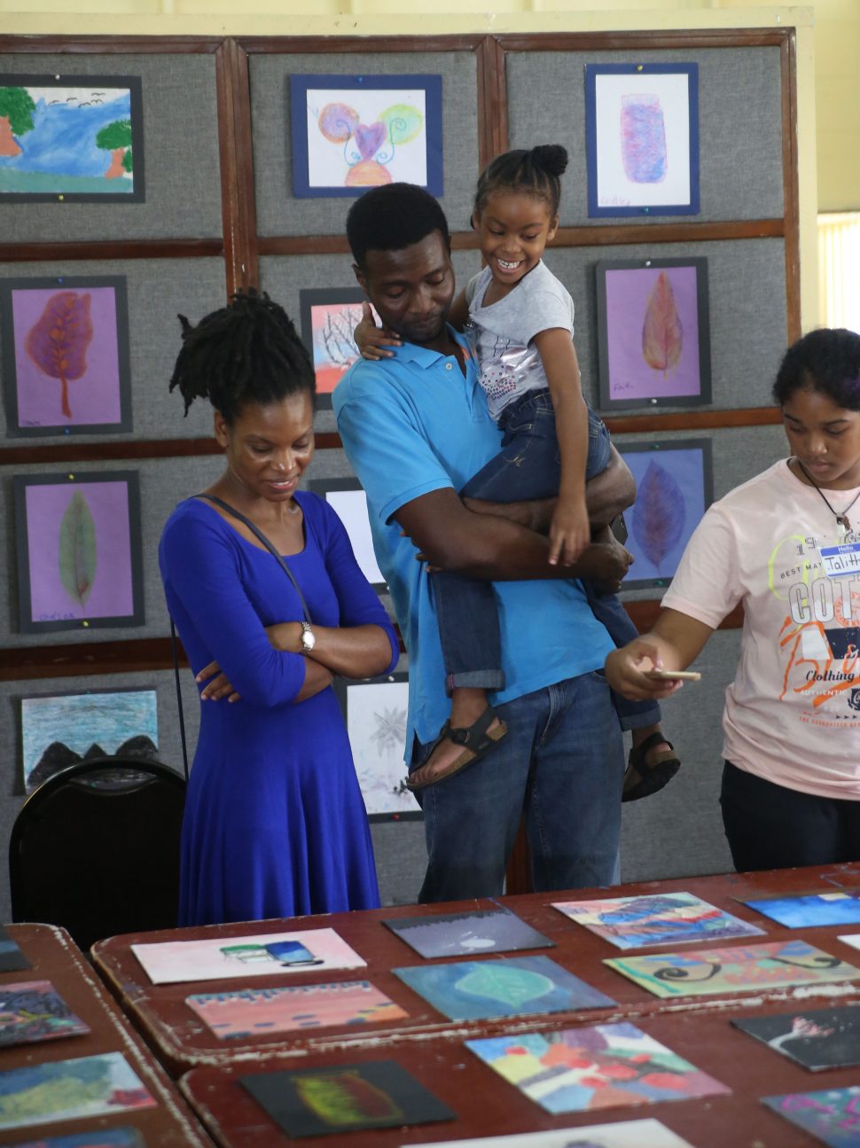 Proud artist: A child proudly showing her parents one of her pieces at a children’s art exhibition that was hosted on Friday at the Carifesta Sports Complex, following the conclusion of a two-week art workshop. (Terrence Thompson photo)