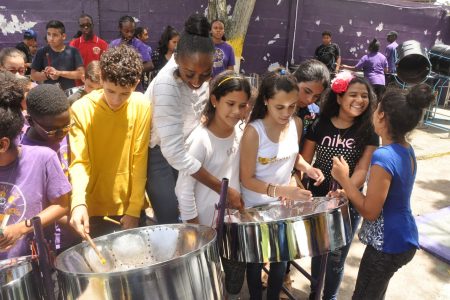 Miss World Trinidad and Tobago Tya Janè Ramey plays pan with some Venezuelan migrant children of the La Romain Migrant Support Group at the Golden Hands Pan Orchestra yesterday.