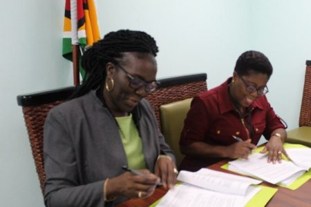 Permanent Secretary of the Ministry of the Presi-dency, Abena Moore (left) and Commissioner of the Protected Areas Commission,  Denise Fraser signing the agreement in the Boardroom of the Ministry of the Presidency. (Ministry of the Presidency photo)