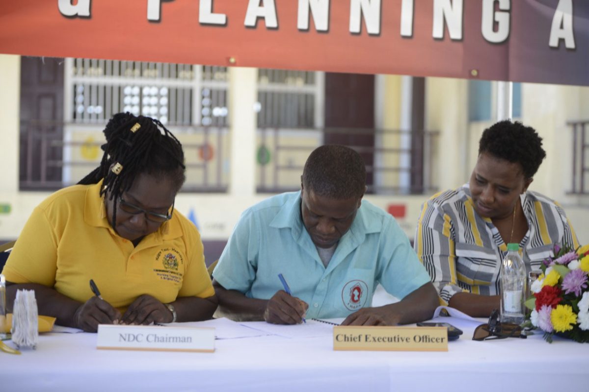Malgre Tout/Meer Zorgen NDC Chair Dolis Eadies (left) and Chief Executive Officer of the CH&PA Lelon Saul (centre) sign a Memorandum of Understanding to facilitate the NDC’s management of several housing schemes in the area while Minister Annette Ferguson (right) looks on. (Photo by Terrence Thompson) 