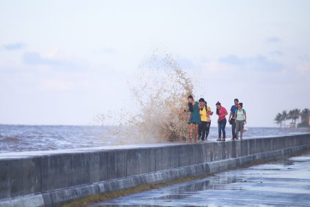 A group of young people had their afternoon stroll punctuated by a salty spray as waves crested the Georgetown’s sea wall during yesterday’s high tide. (Photo by Terrence Thompson)