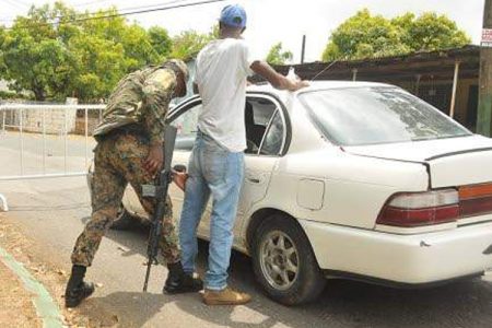 Jamaica Defence Force soldier searches a motorist at a checkpoint on Sevens Road in Clarendon, hours after the state of public emergency was declared in the parish.