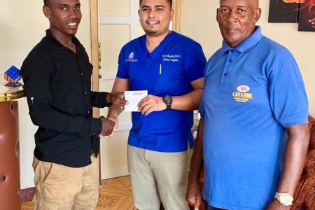  Balram Narine (left) receives his sponsorship from Smile Guyana’s Dr Dhanraj Budhai in the presence of his coach, Randolph Roberts.
