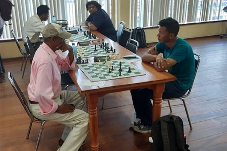 Veteran chess player and former president of the Guyana Chess Federation Errol Tiwari, with cap, is a picture of concentration during his second round match against Steve Leung.
