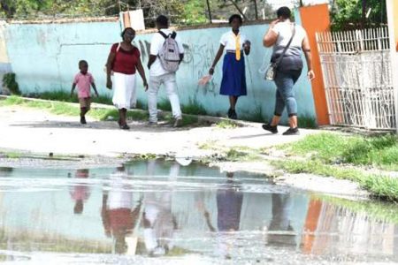Residents walk by a pool of sewage water on a street in Twickenham Park housing scheme in St Catherine, yesterday.