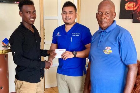 Dr Dhanraj Budhai (center) hands over the sponsorship to cyclist, Balram Narine in the presence of his coach, Randolph Roberts.
