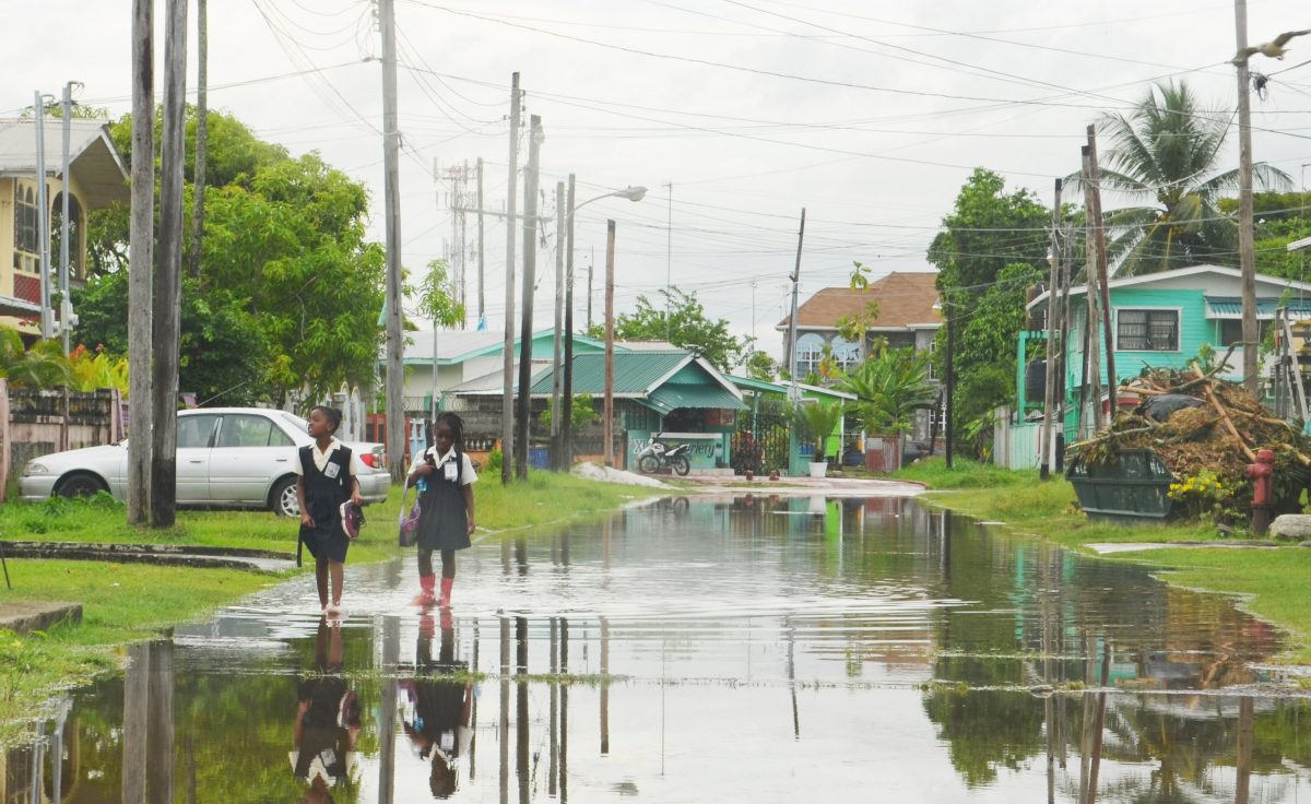 Two school girls navigate their way through a flooded street in Festival City, North Ruimveldt. (Photo by Orlando Charles) 
