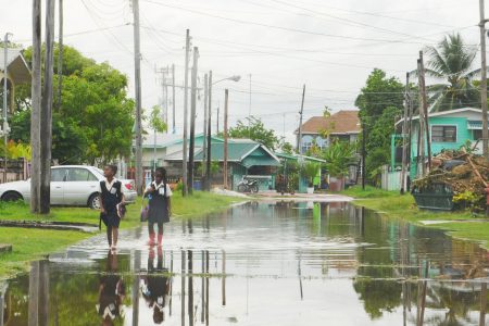 Two school girls navigate their way through a flooded street in Festival City, North Ruimveldt. (Photo by Orlando Charles) 