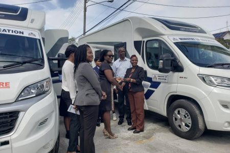 Minister of Education Nicolette Henry (left) handing the keys of the two Mobile Psychosocial Units to Guidance and Counselling Officer Wendy Collins while other ministry staff look on. 