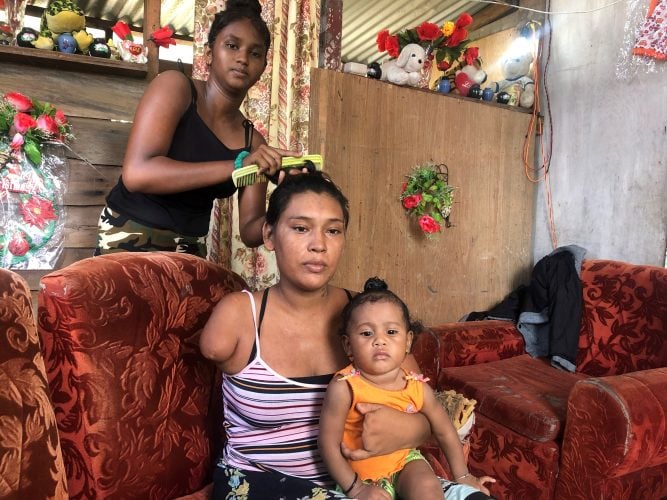 Natasha Houston holding her baby while her neighbour combs her hair.