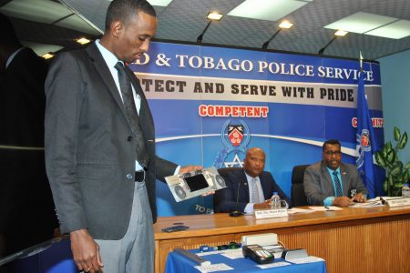 Ag. Cpl. Verne DuBois displays an ATM speaker panel with a cell phone and extra batteries attached used by fraudsters to record bank card Information and pin numbers and make duplicate cards. Looking on are Ag. Supt. Wayne Mystar, centre, and ASP Curtis Julien