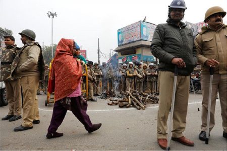 A woman carries her child as she walks past police in riot gear in a street in Meerut, in the northern state of Uttar Pradesh, India, December 27, 2019. REUTERS/Adnan Abidi