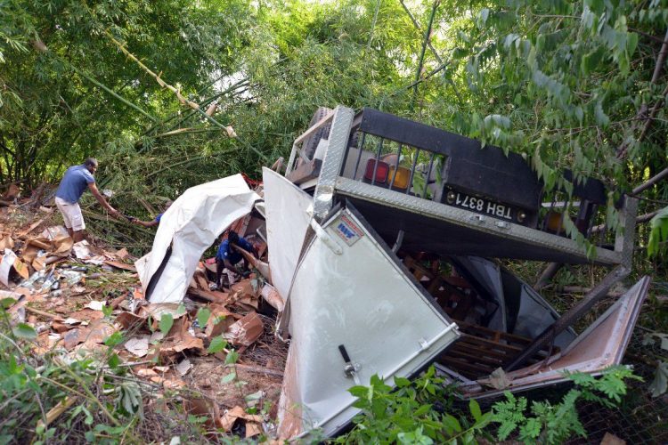 People are seen going through the cargo which spilled onto the cliffside off the Lady Young Road after a deliverry truck rolled down the cliff yesterday afternoon. (Inset) Fire officials remove the body of driver Johnald Smith who died in the crash.