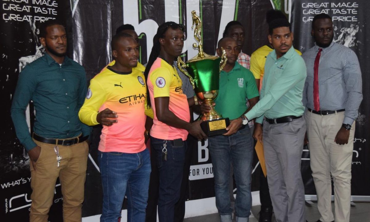 Okeemie Edwards of Friendship collecting the championship trophy from 592 Beer Brand Manager in the presence of several teammates at the official presentation ceremony 
