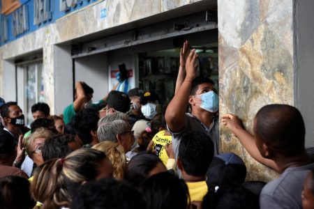 An employee tries to close the shutters of a pharmacy as people crowd around it trying to buy surgical masks and disinfectant gel after the first case of a fast-spreading new coronavirus was confirmed in the country in Guayaquil, Ecuador yesterday. (Reuters/Santiago Arcos)