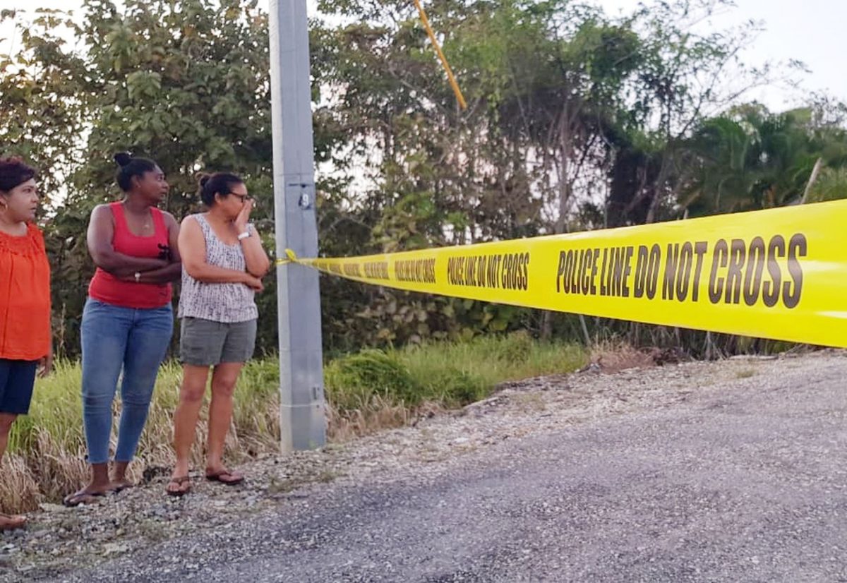 Curious onlookers stand beyond the police tape at the scene of the double murder in Nia Valley Auditorium in Matilda Gardens, Princes Town, yesterday.