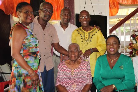 Pearl  Gravesande (seated at left) surrounded by three of her sons, her daughter-in-law and Minister Nicolette Henry (seated at right) (Ministry of Education photo)