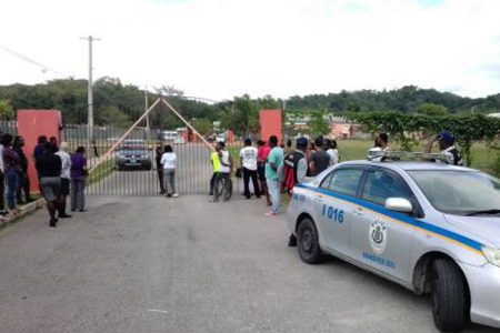 A police vehicle parked outside the gates of the Rhodes Hall High School as curious onlookers gather following the murder of the bus driver on the compound this afternoon - Hopeton Bucknor photo