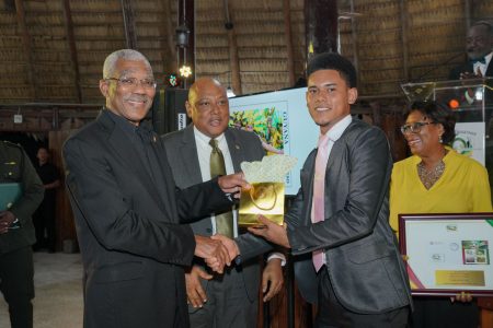 President David Granger (left) receives a token from 21-year-old Delon Craig, who designed one side of the 50th Republic Anniversary gold commemorative medallion. Also photographed are Minister of Natural Resources, Raphael Trotman (centre) and Minister of Public Telecommunications,  Catherine Hughes. (Ministry of the Presidency photo)
