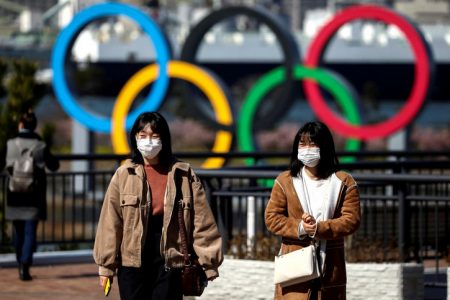 People wearing protective face masks, following an outbreak of the coronavirus, are seen in front of the Giant Olympic rings at the waterfront area at Odaiba Marine Park in Tokyo, Japan, yesterday. REUTERS/Athit Perawongmetha
