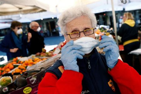 Owner of a fruit stall at Campo de' Fiori market adjusts a protective face mask on the second day of an unprecedented lockdown across all of the country, imposed to slow the outbreak of coronavirus, in Rome, Italy March 11, 2020. REUTERS/Guglielmo Mangiapane