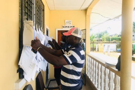 Final check: This resident of Soesdyke, along with two others, were checking to ensure their names were on the Official List of Electors at one of the polling stations at Soesdyke yesterday morning. (David Papannah photo)
