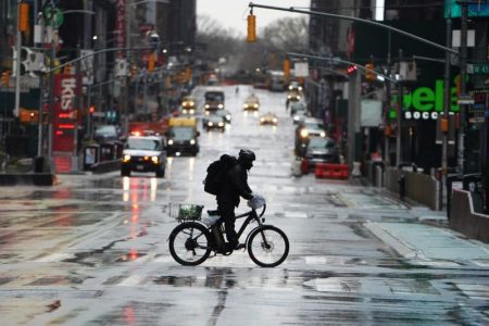 A delivery person rides their bike across 7th Avenue in a mostly deserted Times Square following the outbreak of Coronavirus disease (COVID-19), in the Manhattan borough of New York City, New York, U.S., March 23, 2020. REUTERS/Carlo Allegri