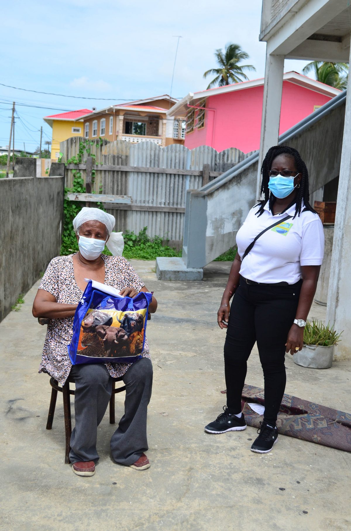 A recipient (seated) of one of the hampers distributed yesterday by the Lodge Housing Scheme Beautification Group to vulnerable members of the community. See story on page 13.  (Orlando Charles photo)