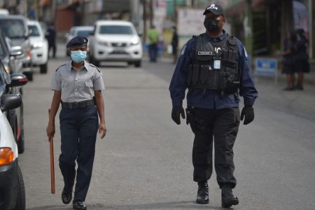 Police officers patrol Mucurapo Street in San Fernando, while observing shoppers at the San Fernando Market yesterday, to ensure they kept social distancing to five-feet in a public space. -Photo: DEXTER PHILIP 