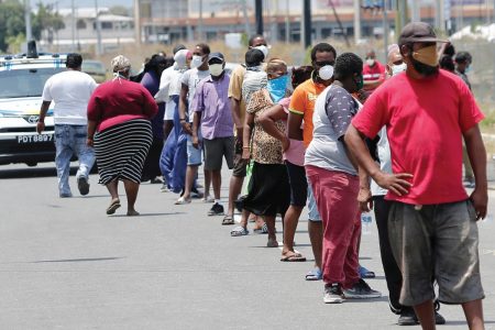 People wait in line to collect hampers at the Barakah Grounds in Chaguanas yesterday.