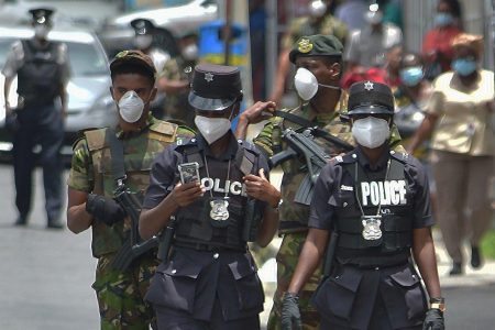 Police officers and members of the defence force walk along Pointe-a-Pierre Road in San Fernando, during a joint-patrol on Tuesday. -Photo: DEXTER PHILP 