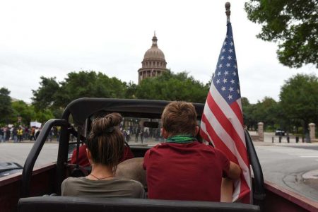 People sit in a car with an American flag as protesters against the state’s extended stay-at-home order to help slow the spread of the coronavirus disease (COVID-19) demonstrate at the Capitol building in Austin, Texas, U.S., April 18, 2020. REUTERS/Callaghan O’Hare