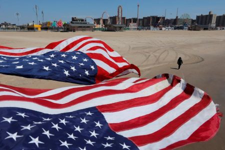 A person walks along the sand under flags of the United States of America at the Coney Island beach during the outbreak of the coronavirus disease (COVID-19) in Brooklyn, Manhattan, New York City, New York, U.S., April 19, 2020. REUTERS/Andrew Kelly