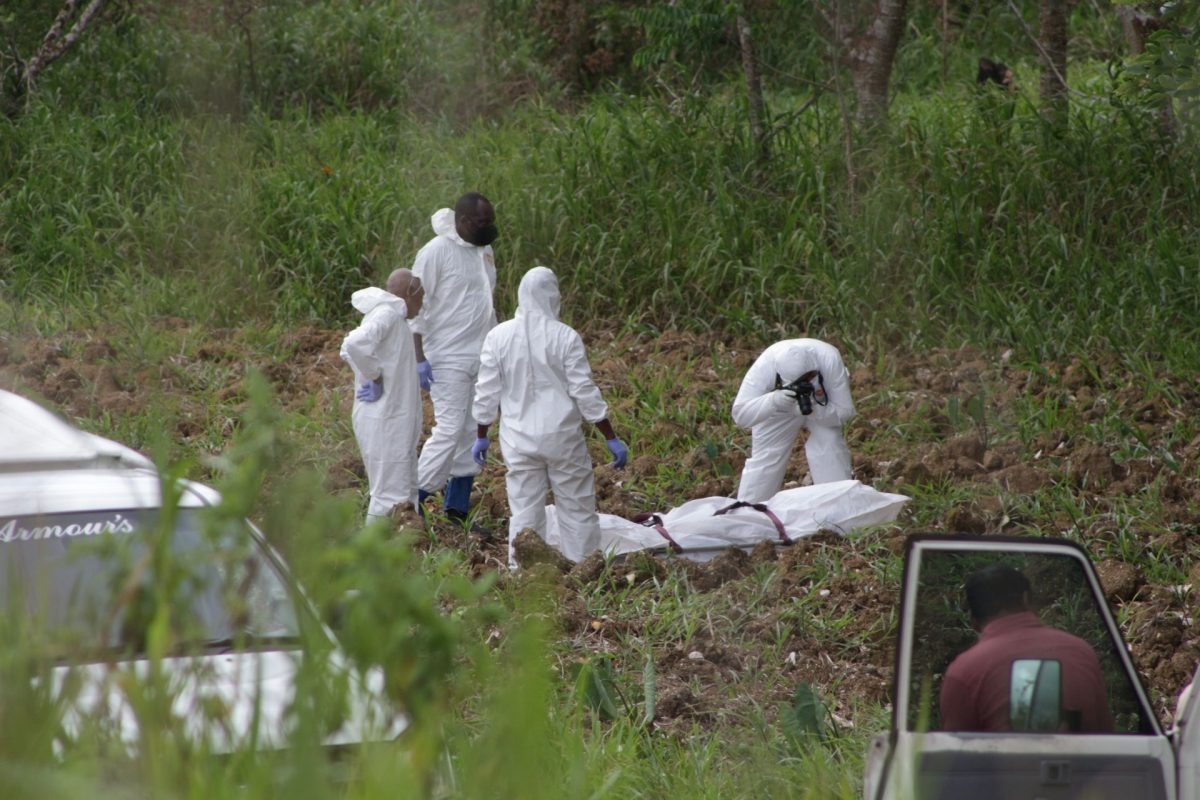 A Crime Scene Investigator (CSI)  photographs the body of one of the victims in a quadruple murder at Daly Road, New Grant yesterday as undertakers look on.