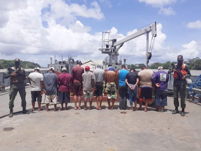 Venezuelan soldiers guard a group of human traffickers after they rescued 79 people who were to be brought to Trinidad in a camp along the Orinoco Delta yesterday.