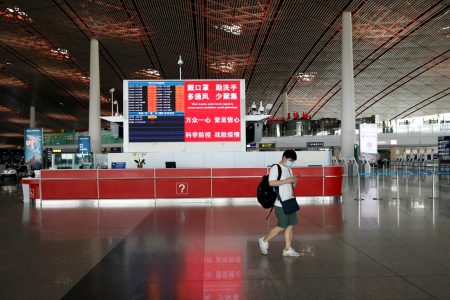 A man wearing a face mask walks past a counter with a display showing flight information and a message on preventive measures against the coronavirus disease (COVID-19), at the departure hall of Beijing Capital International Airport after scores of domestic flights in and out of the Chinese capital were cancelled, in Beijing, China June 17, 2020. REUTERS/Carlos Garcia Rawlins