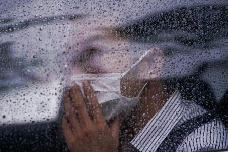 A man wearing face mask sits inside a car during a raining day in Shanghai, following the coronavirus disease (COVID-19) outbreak, China June 18, 2020. Picture taken through a window glass REUTERS/Aly Song