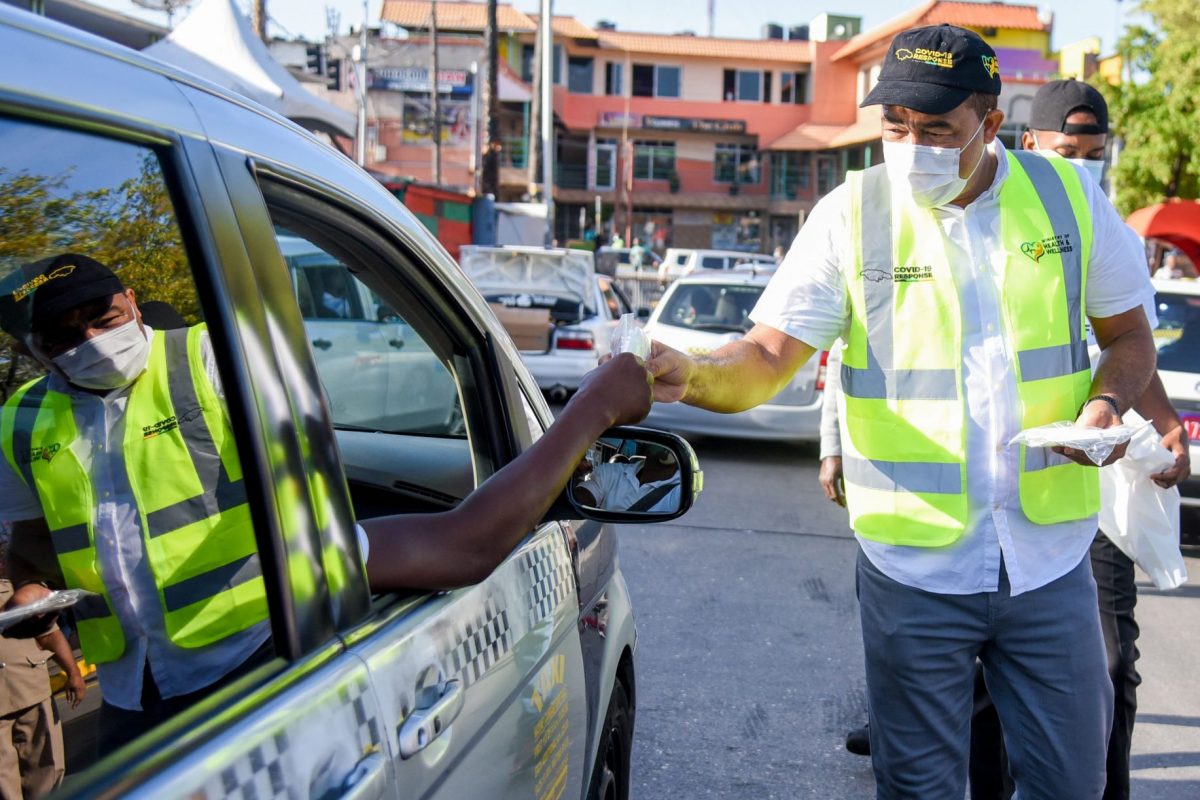 Health and Wellness Minister, Dr. the Hon. Christopher Tufton (right), hands a mask to a taxi operator, during a public awareness exercise put on by the Ministry on Monday (June 1)
