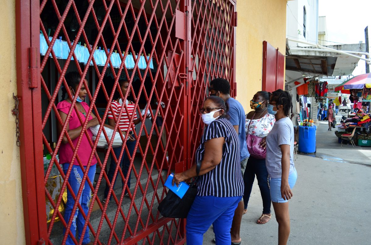 Persons shopping through a closed gate (Photo by Orlando Charles) 