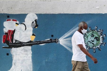 A man walks next to a graffiti depicting a cleaner wearing protective gear spraying viruses with the face of Brazil’s President Jair Bolsonaro amid the coronavirus disease (COVID-19) outbreak, in Rio de Janeiro, Brazil, June 12, 2020. REUTERS/Sergio MoraesReuters