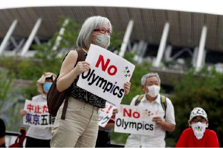 A demonstrator wearing a face mask holds a sign to protest against the Tokyo 2020 Olympic Games a year before the start of the summer games that have been postponed to 2021 due to the coronavirus disease (COVID-19) outbreak, near National Stadium in Tokyo, Japan July 24, 2020. REUTERS/Issei Kato