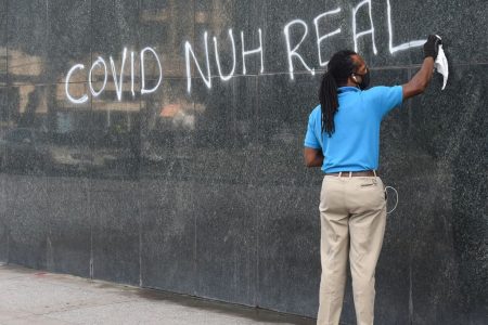 A man cleans a spray-painted sign off a section of the wall on First Citizens’ Independence Square, Port-of-Spain branch yesterday.