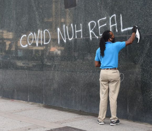 A man cleans a spray-painted sign off a section of the wall on First Citizens’ Independence Square, Port-of-Spain branch yesterday.